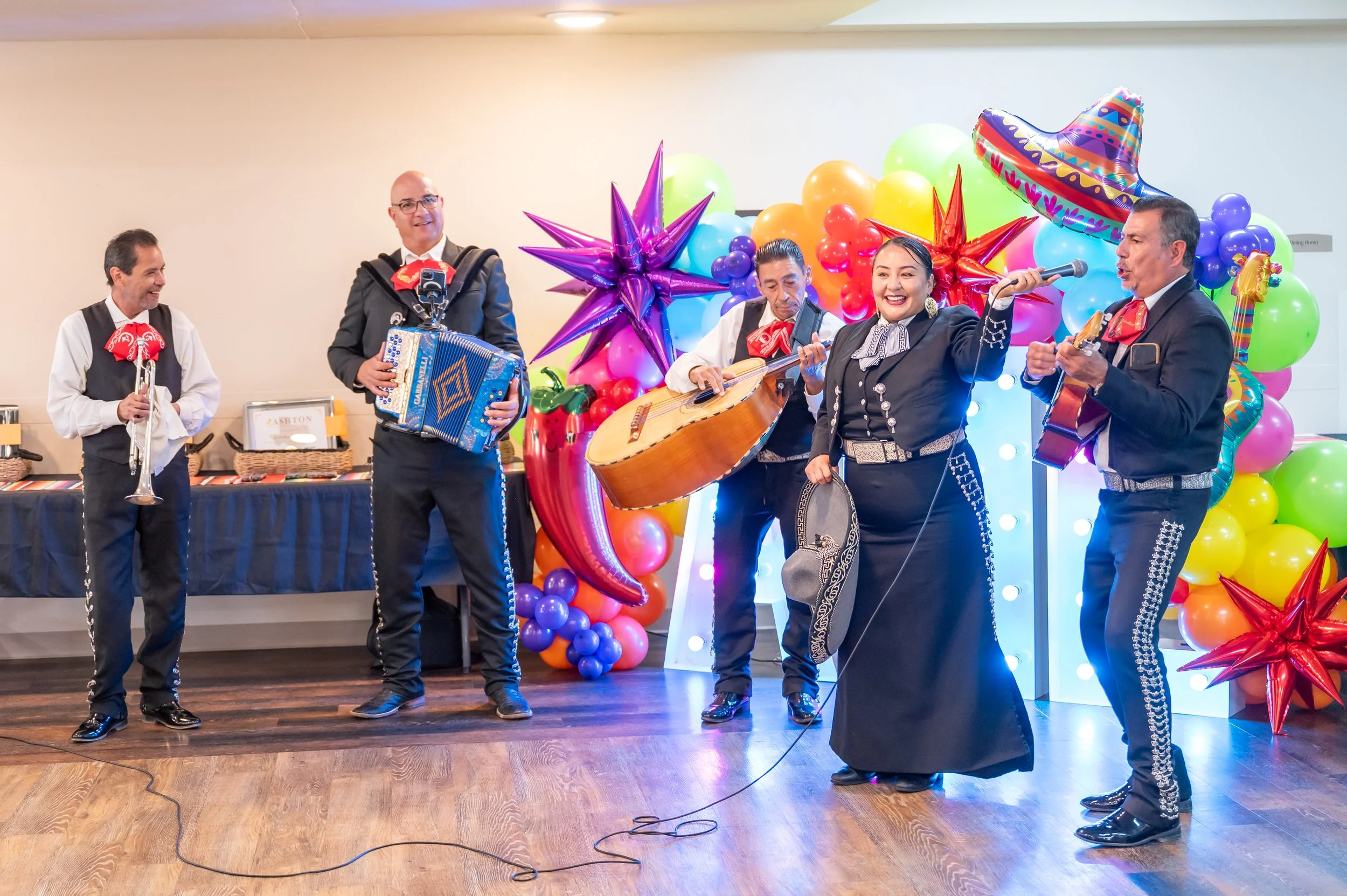 Mariachi band performing at a celebration with colorful balloons and sombrero decorations.