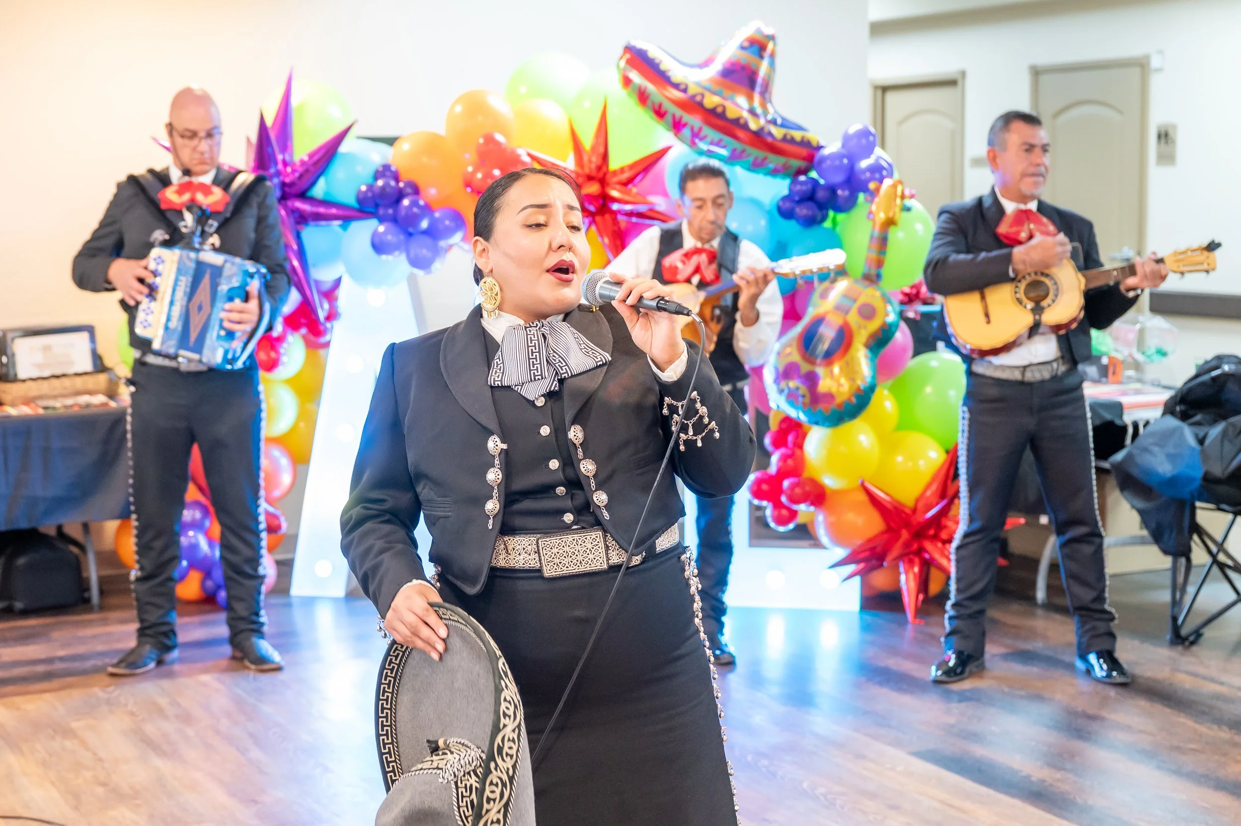 Mariachi band performing at a celebration with colorful balloons and sombreros in the background.