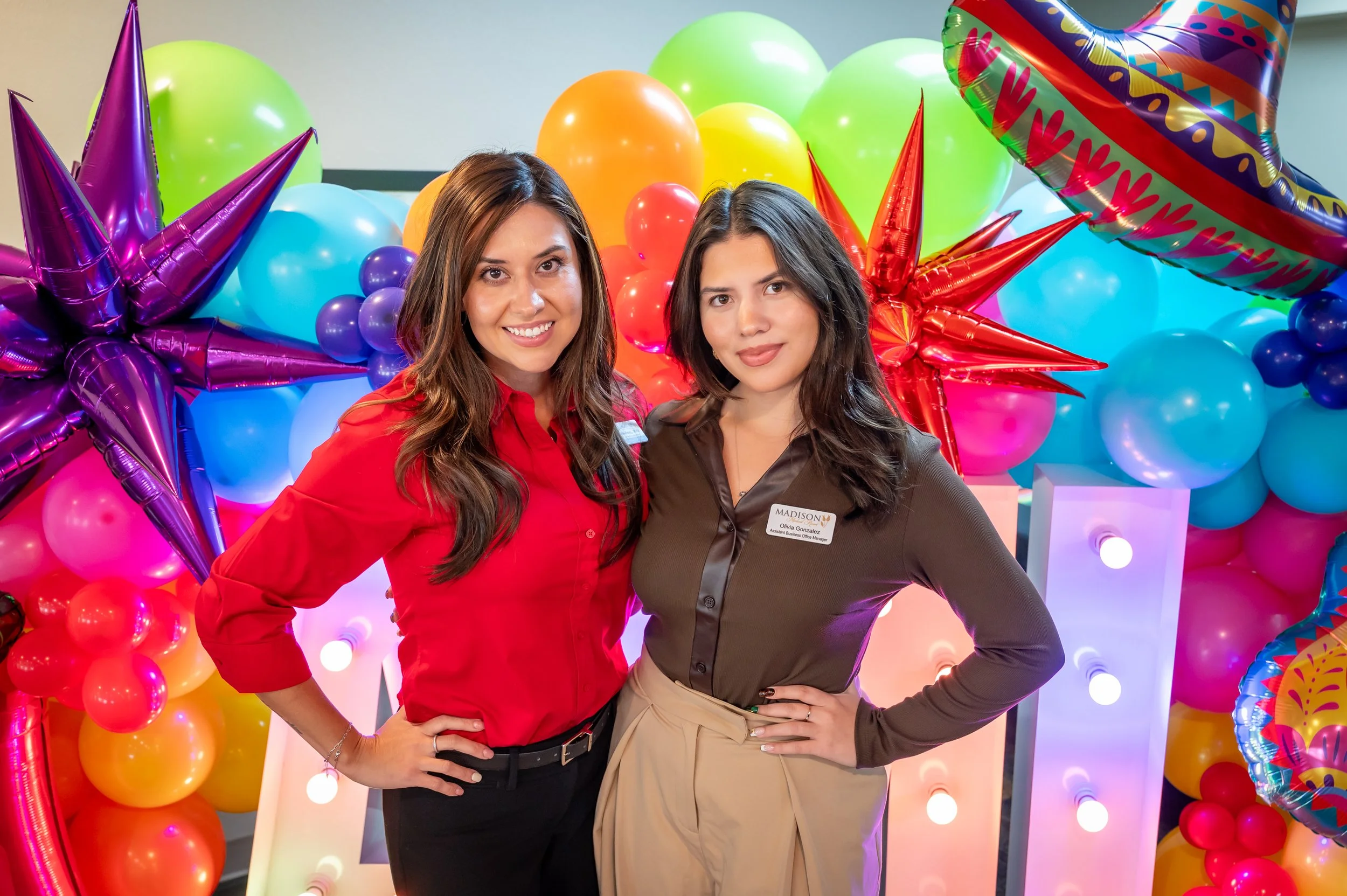 Two women standing in front of colorful balloons and star-shaped balloons at a celebration or party.