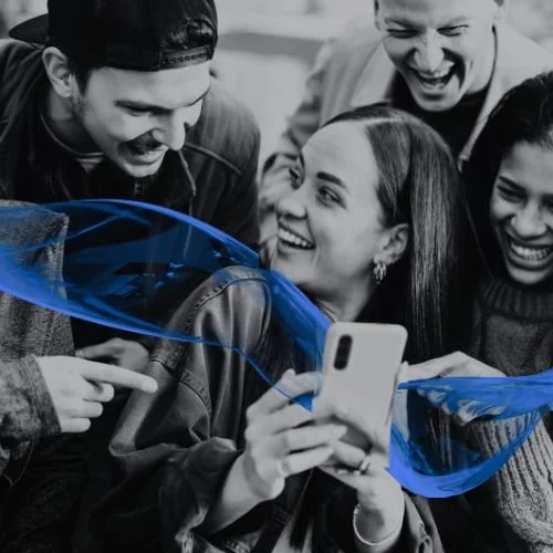 Group of four young people smiling and looking at a smartphone, with a blue light effect on the phone's screen.
