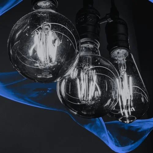 Close-up of three vintage-style incandescent light bulbs hanging from black sockets, with a dark background and a blue wave-like element.