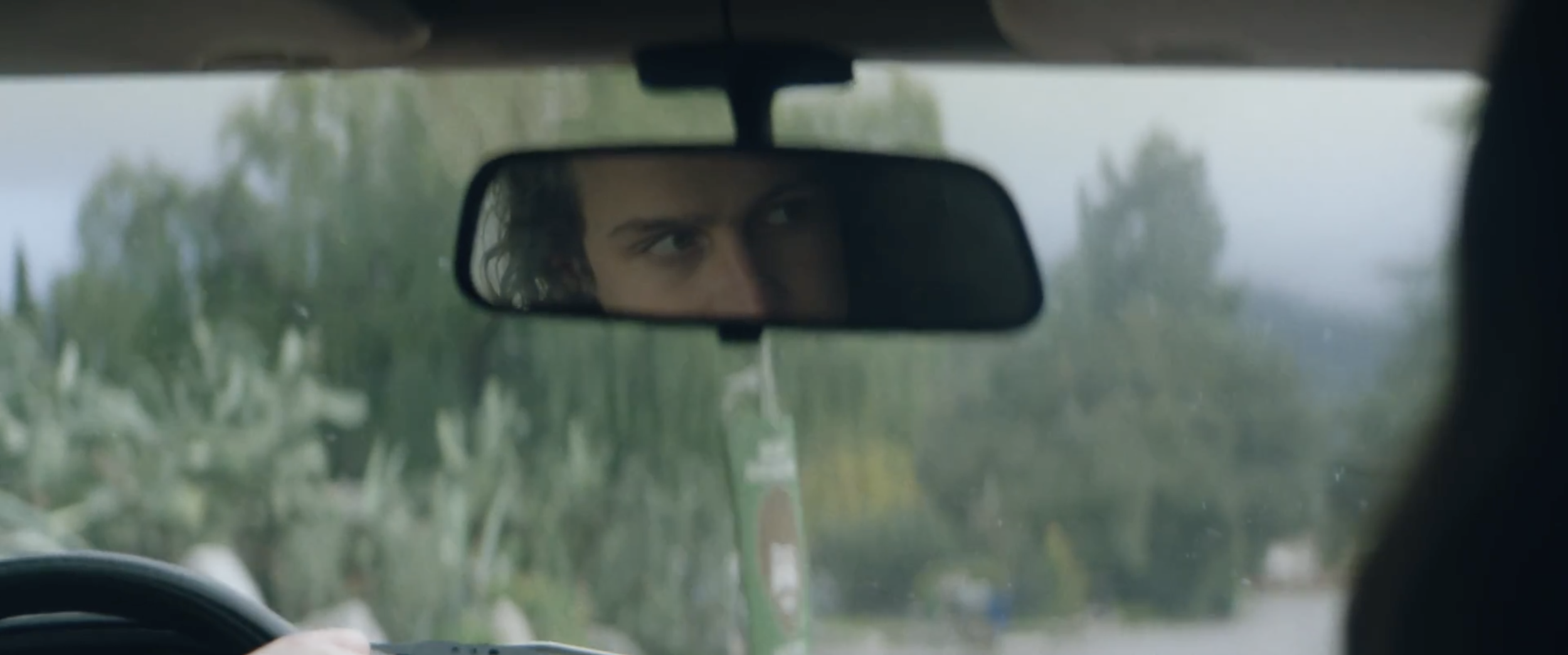 Still from the short film, SILVERTONE. A person with curly brown hair looks ahead in a car rearview mirror.