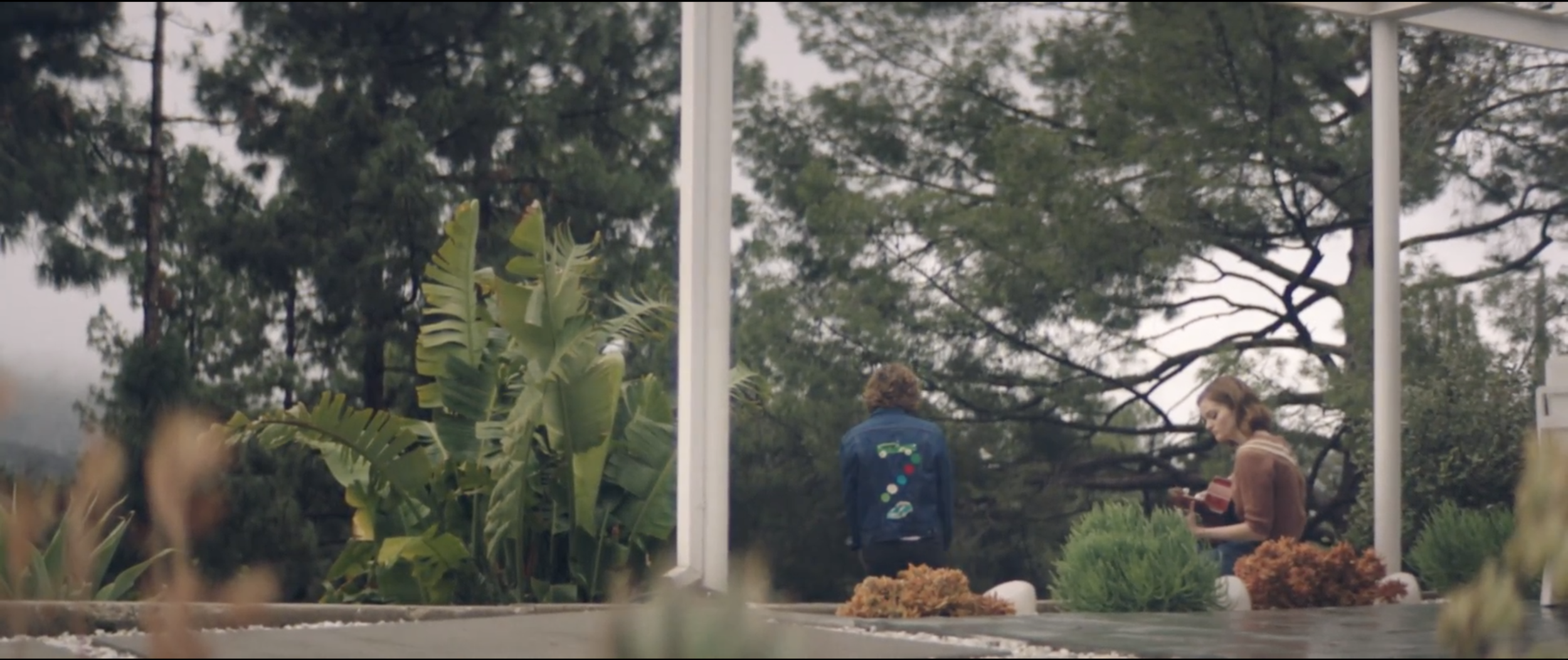 Still from the short film, SILVERTONE. Two people (Kerris Dorsey and Logan Miller) stand outside among trees and plants.