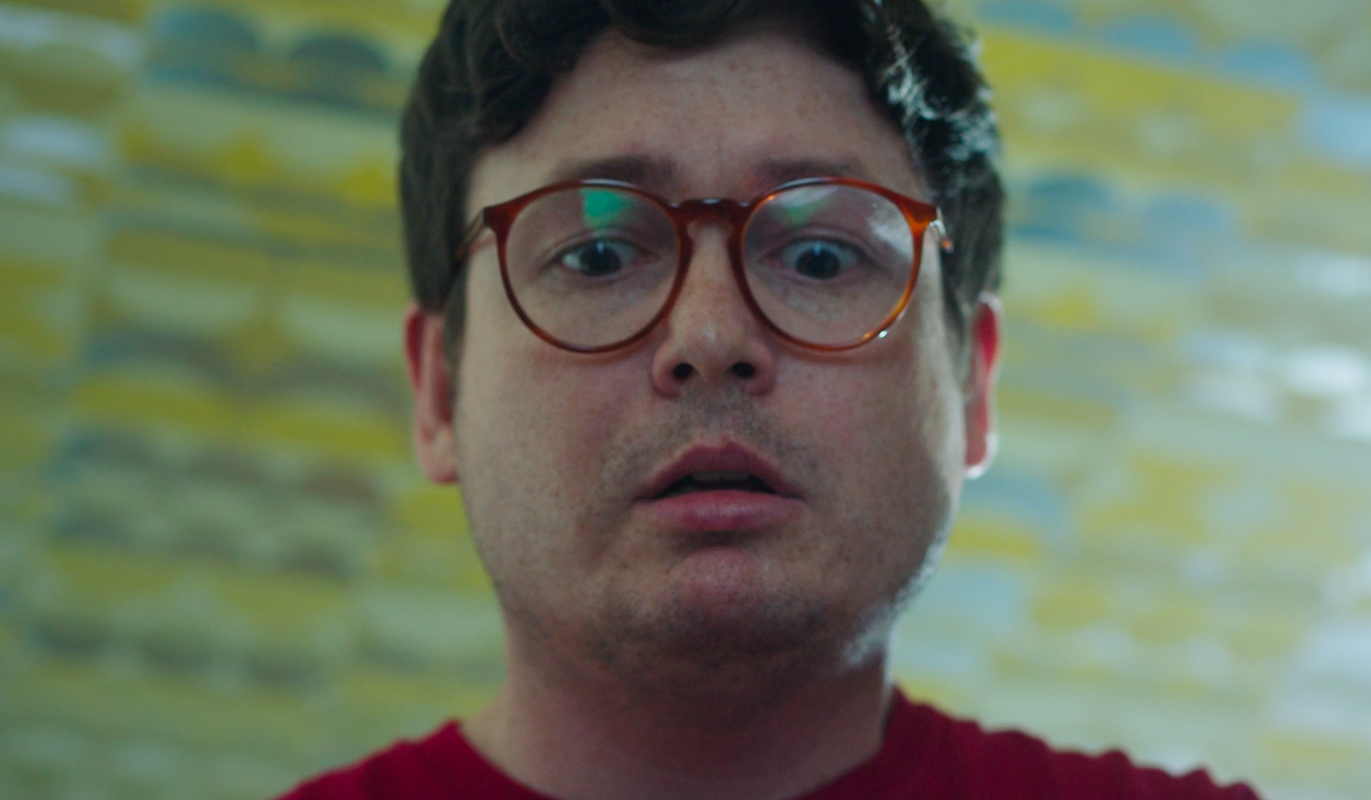 Still from the short film, EXTERMINATOR. A man (Allan McLeod) wearing glasses and a red shirt looks down in horror.