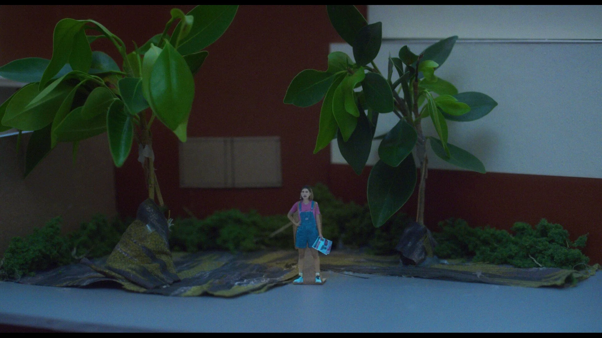 Still from the short film, SUSIE SEARCHES. A miniature version of a young woman (Sophie Kargman) against a high school backdrop.