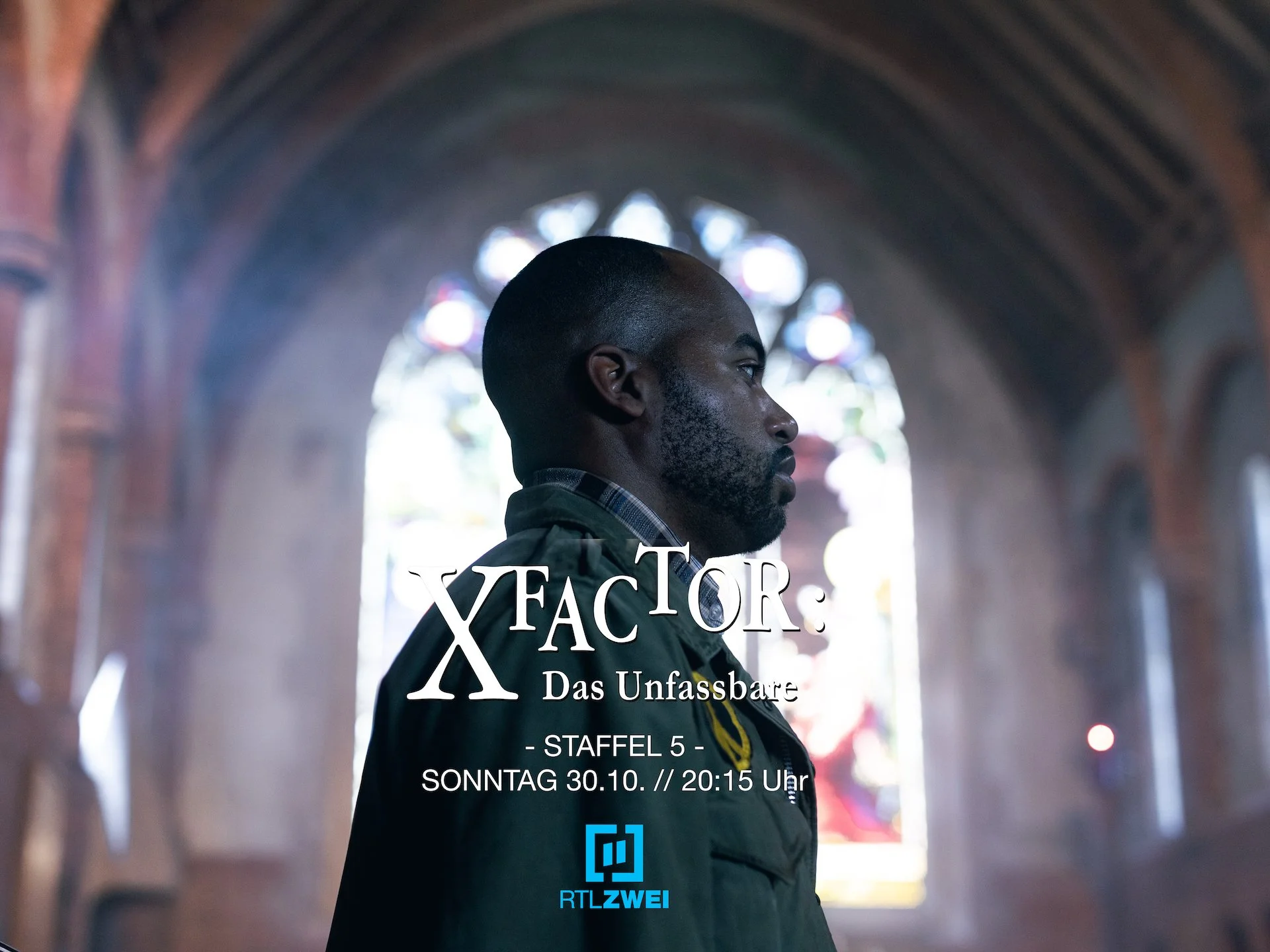 Behind-the-scenes promotional photo from the TV series X FACTOR: DAS UNFASSBARE. Side profile of a bearded man inside a church with a large stained glass window in the background.