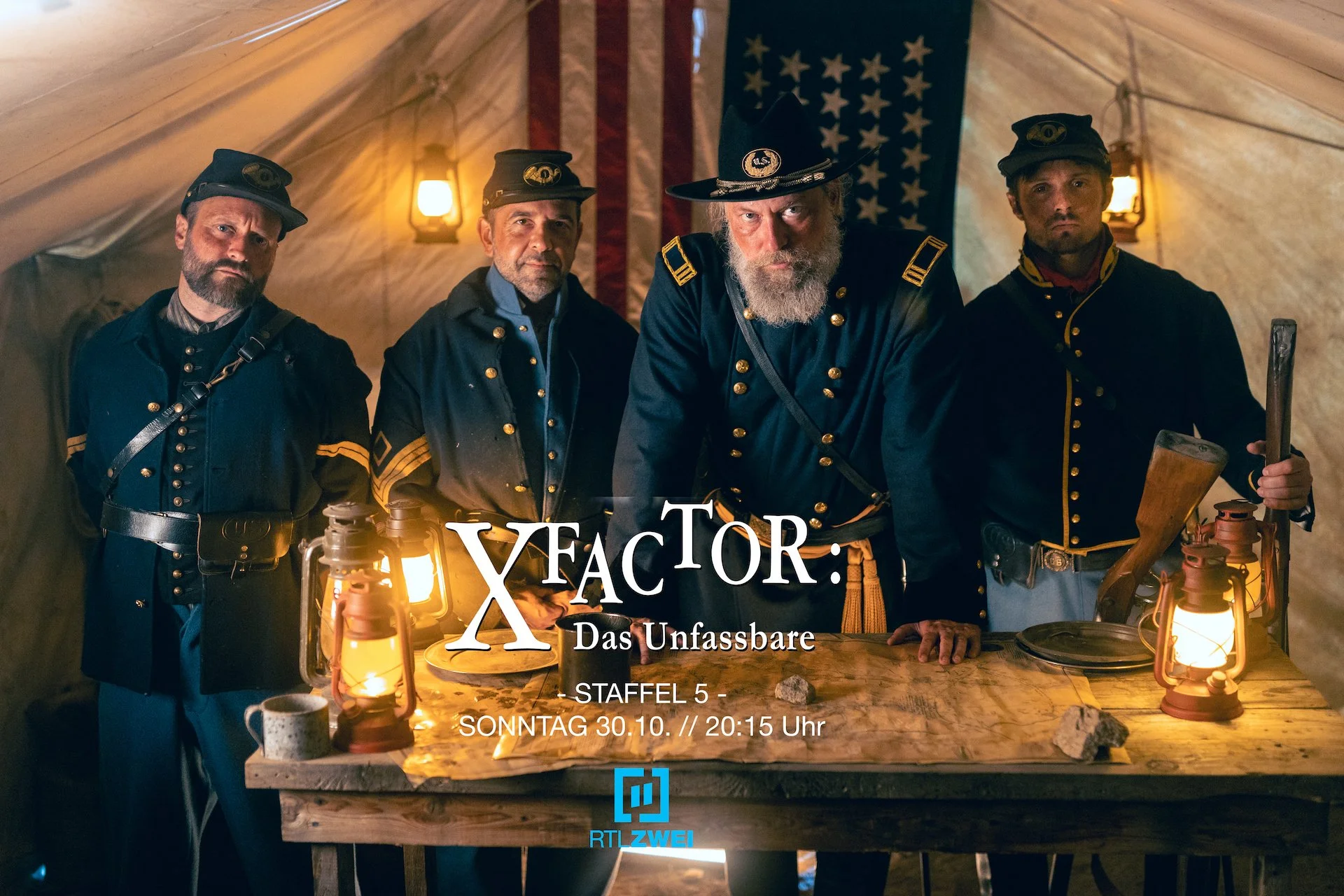 Behind-the-scenes promotional photo from the TV series X FACTOR: DAS UNFASSBARE. Four men dressed as Civil War soldiers stand behind a wooden table with lanterns inside a tent. An American flag hangs in the background.