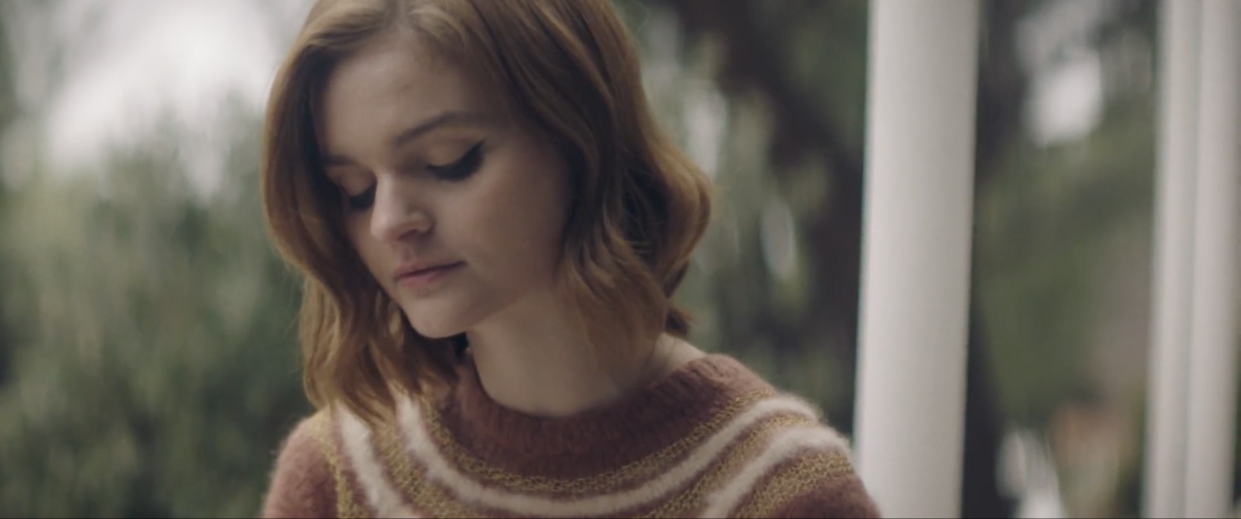Still from the short film, SILVERTONE. A young woman (Kerris Dorsey) wears a cream-striped brown sweater. She sits outside with a contemplative expression.