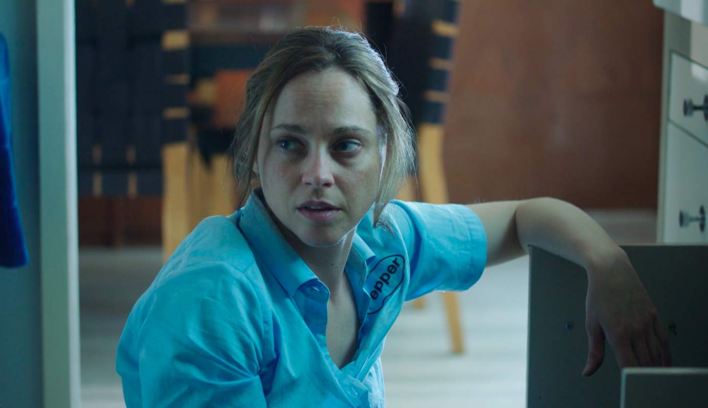 Still from the short film, EXTERMINATOR. A woman (Fiona Dourif) with unkempt hair and a slightly distressed expression wears an exterminator's uniform.