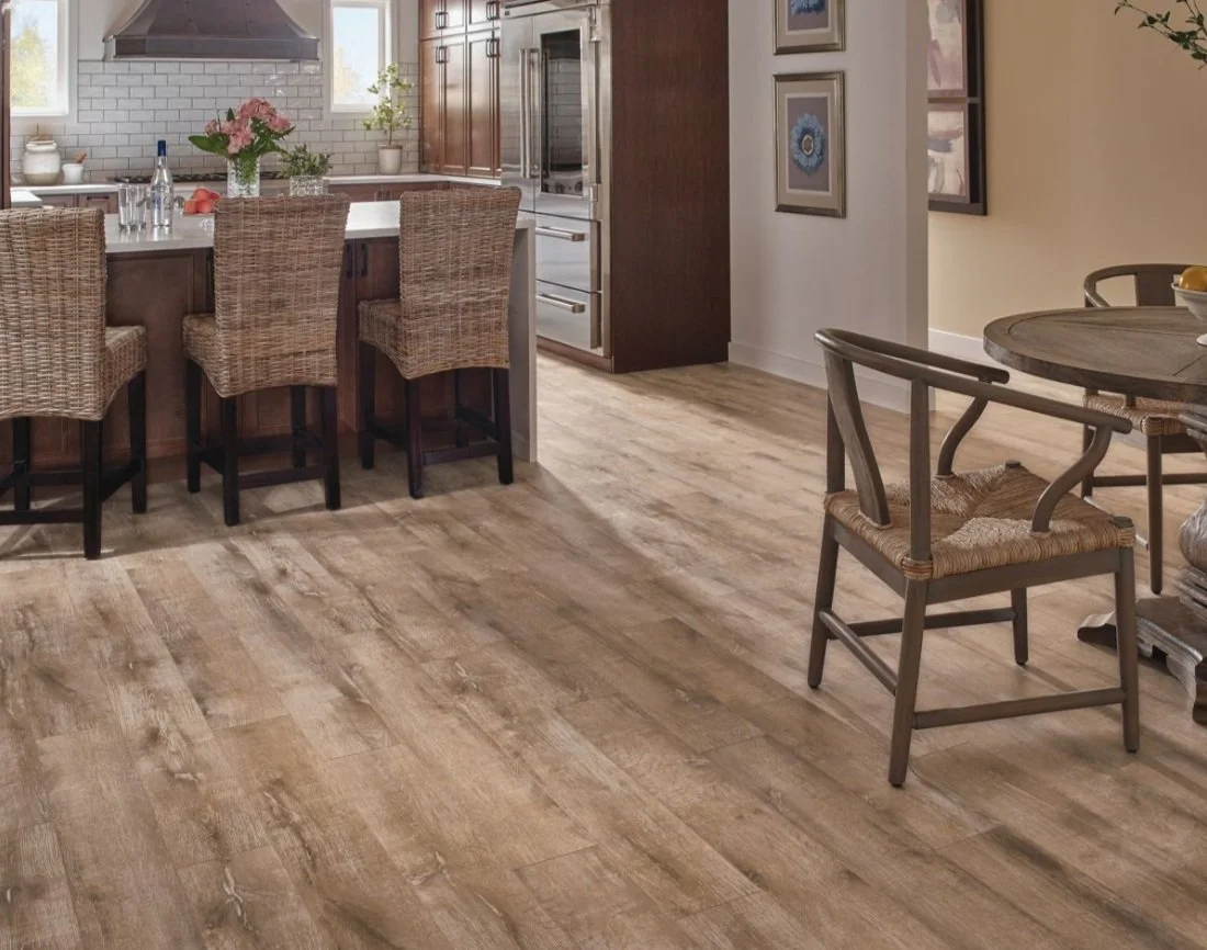 Kitchen and dining area with wood plank flooring, four wicker bar stools at a white counter, a round dining table with woven chairs, and wall art.