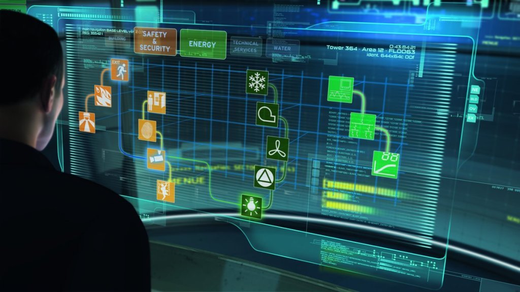 A person looking at a large digital screen displaying a complex interface with icons related to safety, security, energy, and technical services, along with graphs and data.