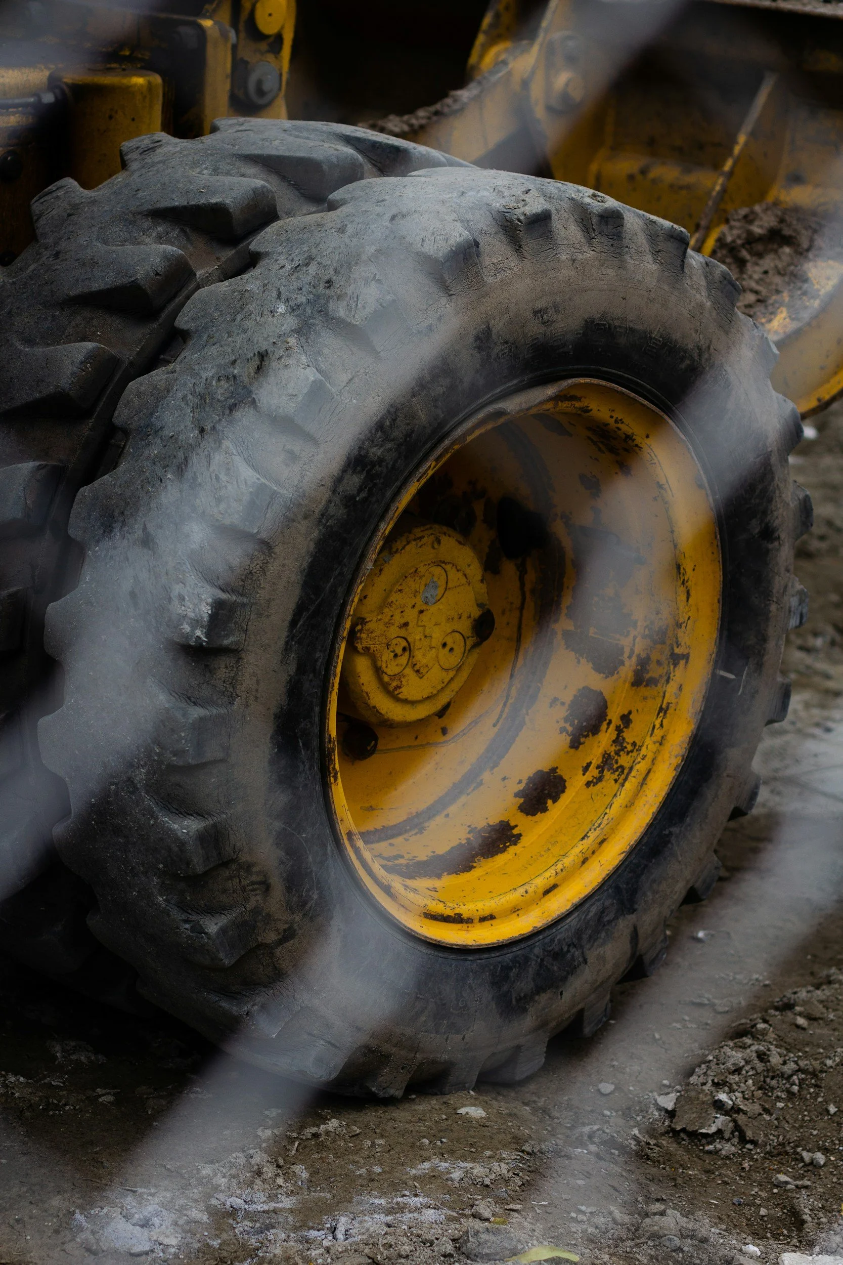 Close-up of a large yellow construction vehicle tire on a muddy ground, with visible dirt and mud on the tire tread.