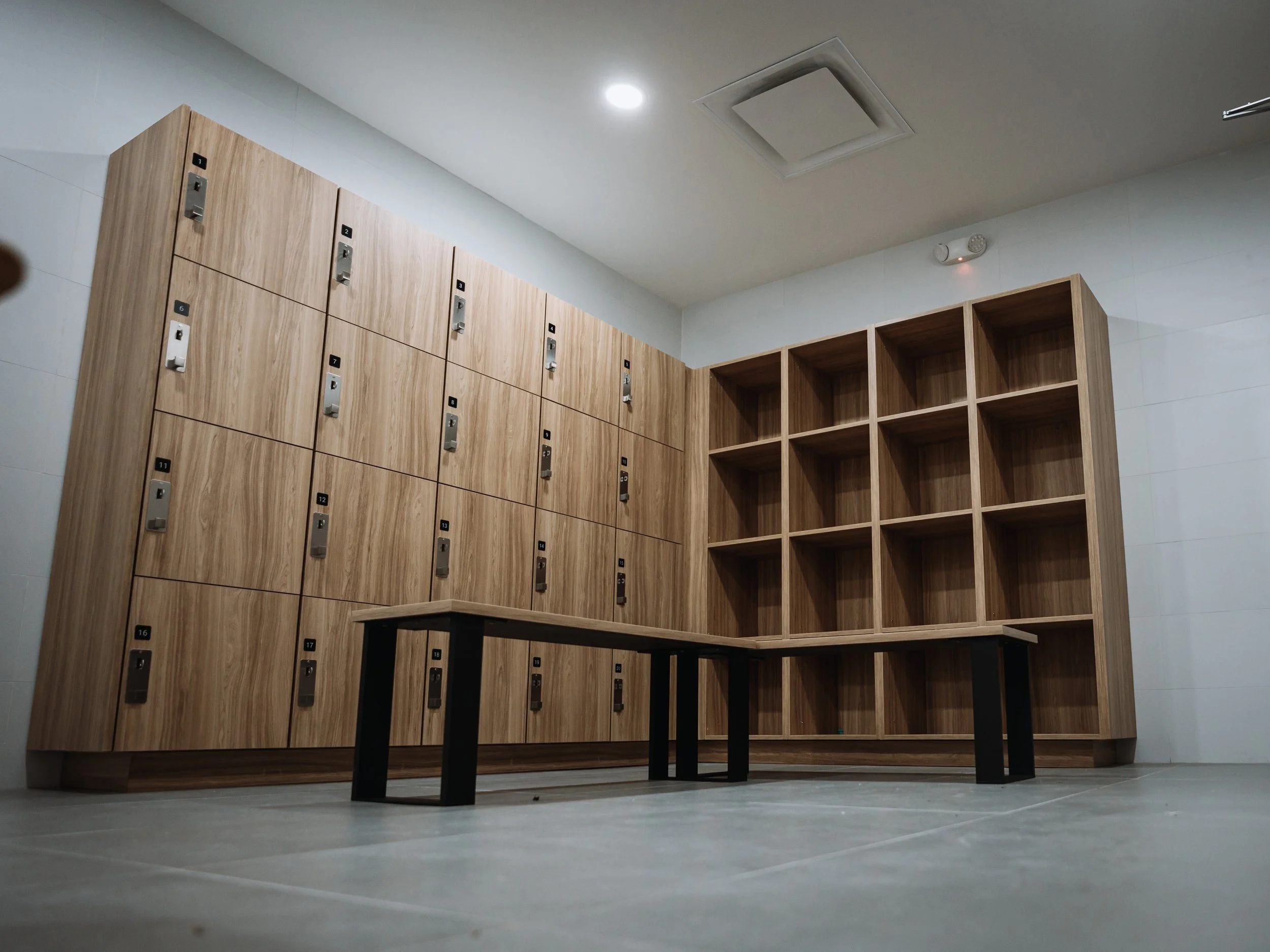 A room with wooden lockers and open cubbies, a small black table, ceiling light, and white walls.