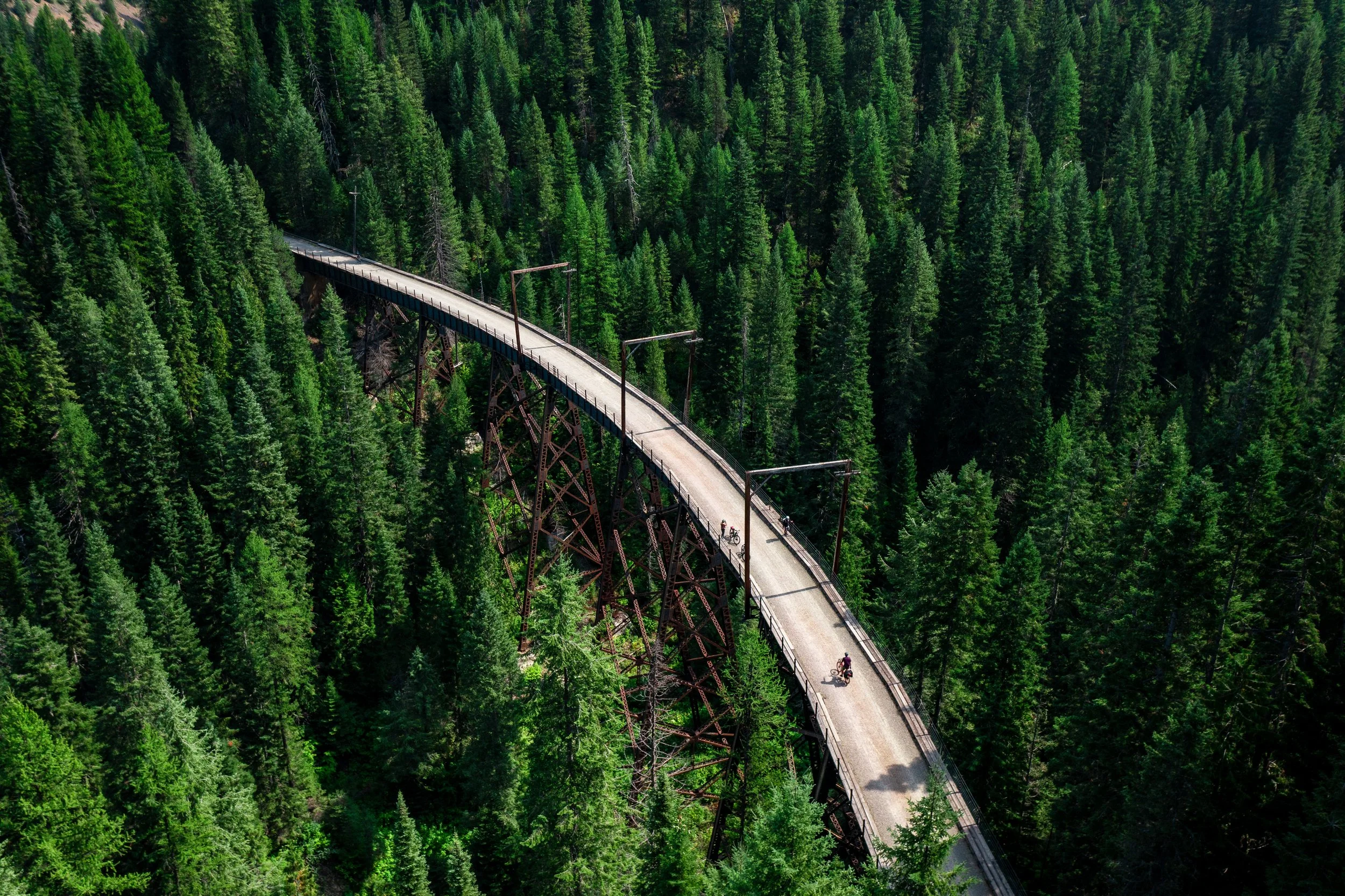 Aerial drone photo of the Route of the Hiawatha Trail in northern Idaho, showing forested mountains, trestles, and bike path below.