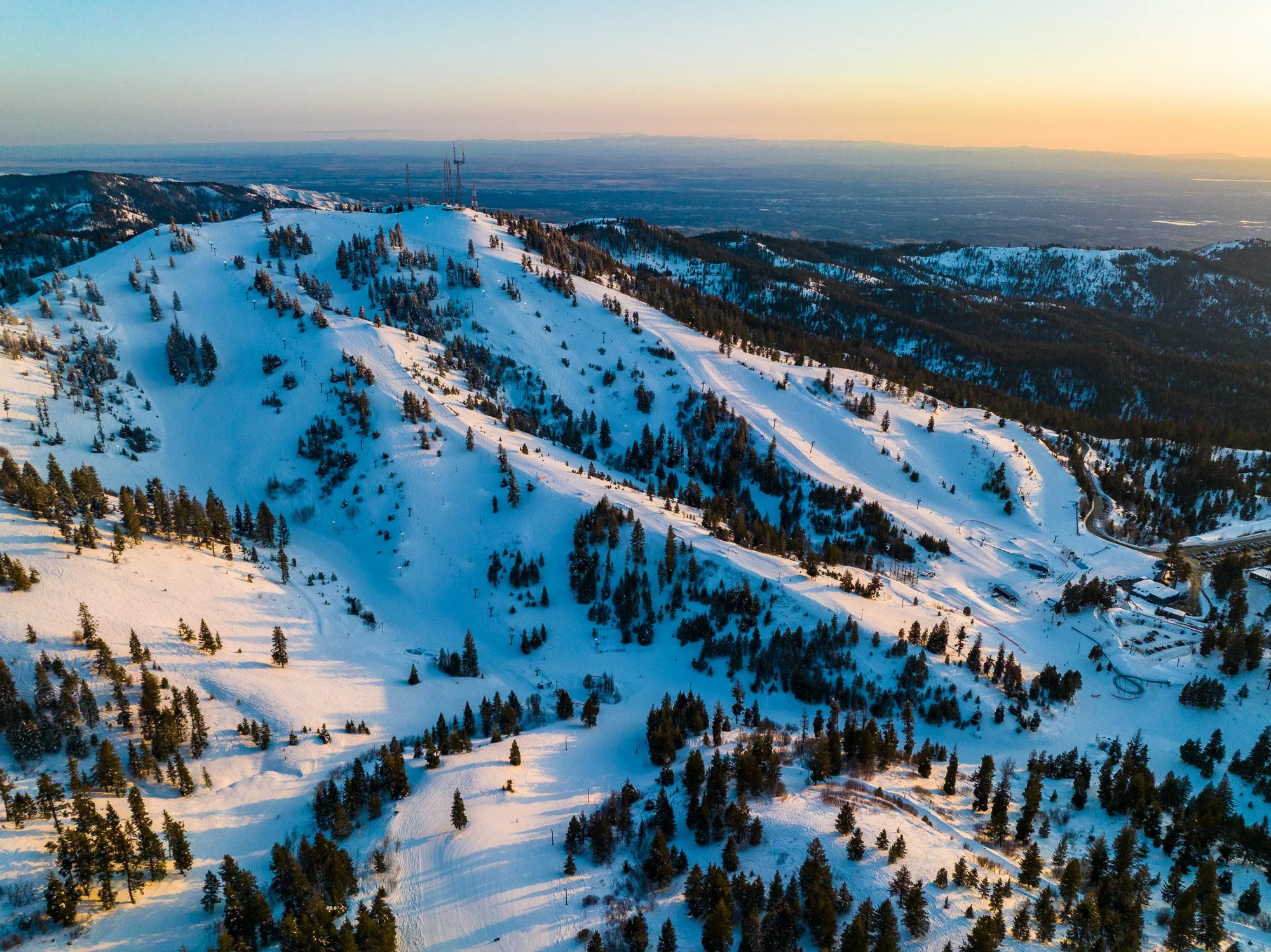 Twilight aerial drone photo of Bogus Basin Ski Resort near Boise, Idaho, with snow-covered slopes and lodge lights glowing.