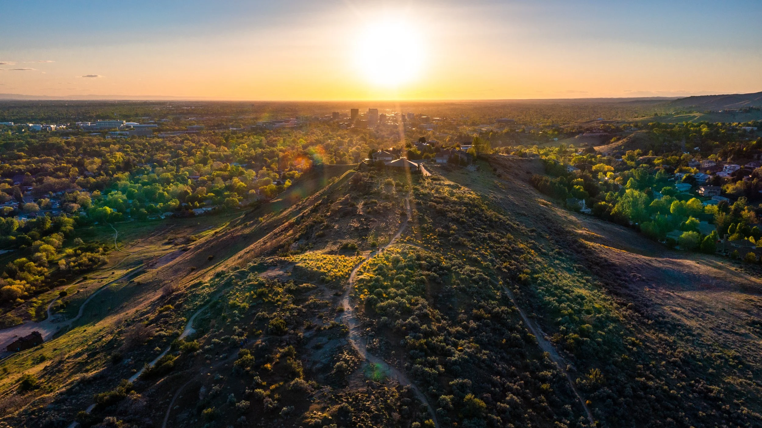 Aerial drone photograph of Boise, Idaho at sunset, captured by Jon Conti Visuals. This 5K image features a luxury home in the foreground overlooking the city skyline and foothills beyond — a cinematic blend of Boise’s residential architecture and the