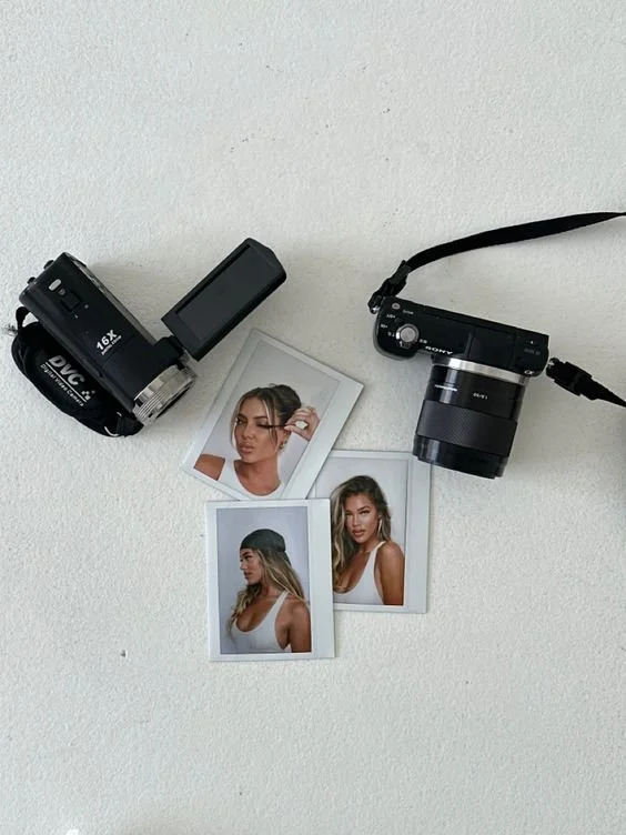 Two cameras on a white surface with three instant photos of a woman in between.