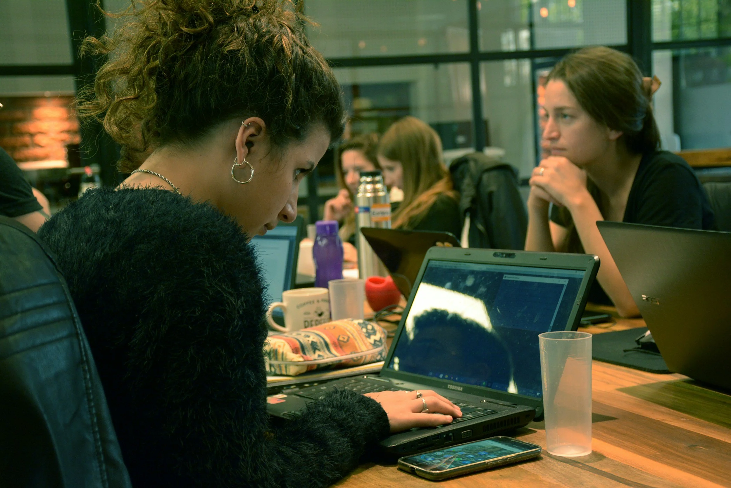 People working on laptops at a communal table in a modern office or coworking space.