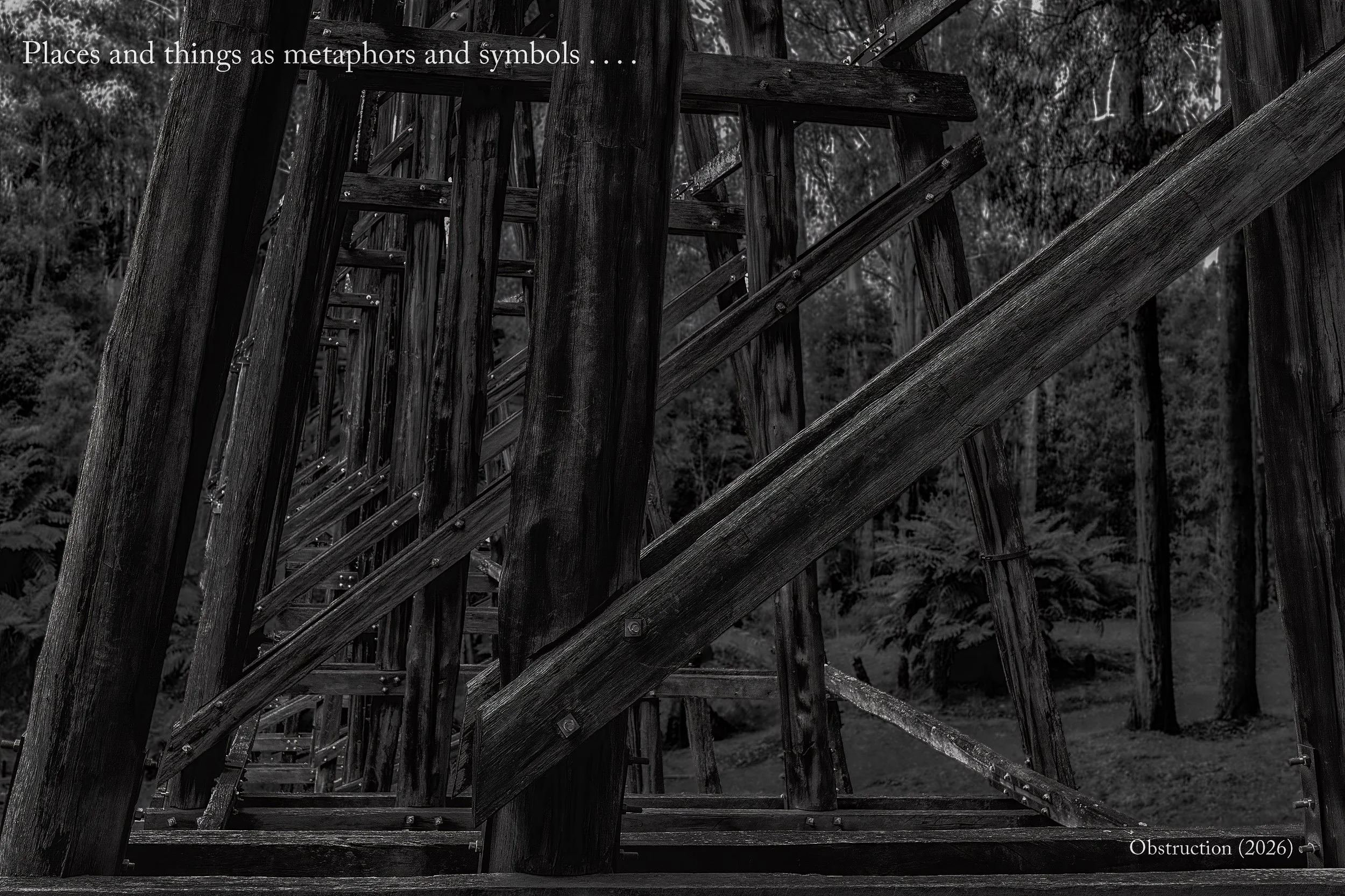 A view looking through the superstructure of an old truss bridge. The caption says Places and things as metaphors and symbols . . . . the title is Obstruction (2026).