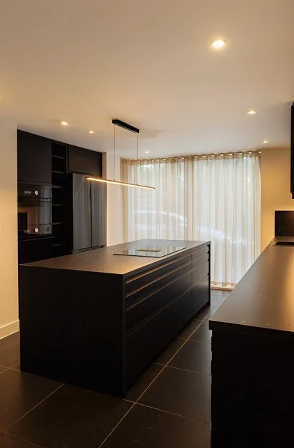 Modern kitchen interior in Henslow Mews, Cambridge, featuring black cabinetry, marble island, and soft natural light filtering through sheer curtains