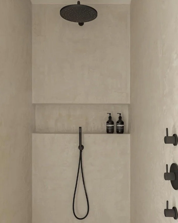 Dubai bathroom with microtopping walls, matte black fixtures, and recessed shelf in a minimalist shower.