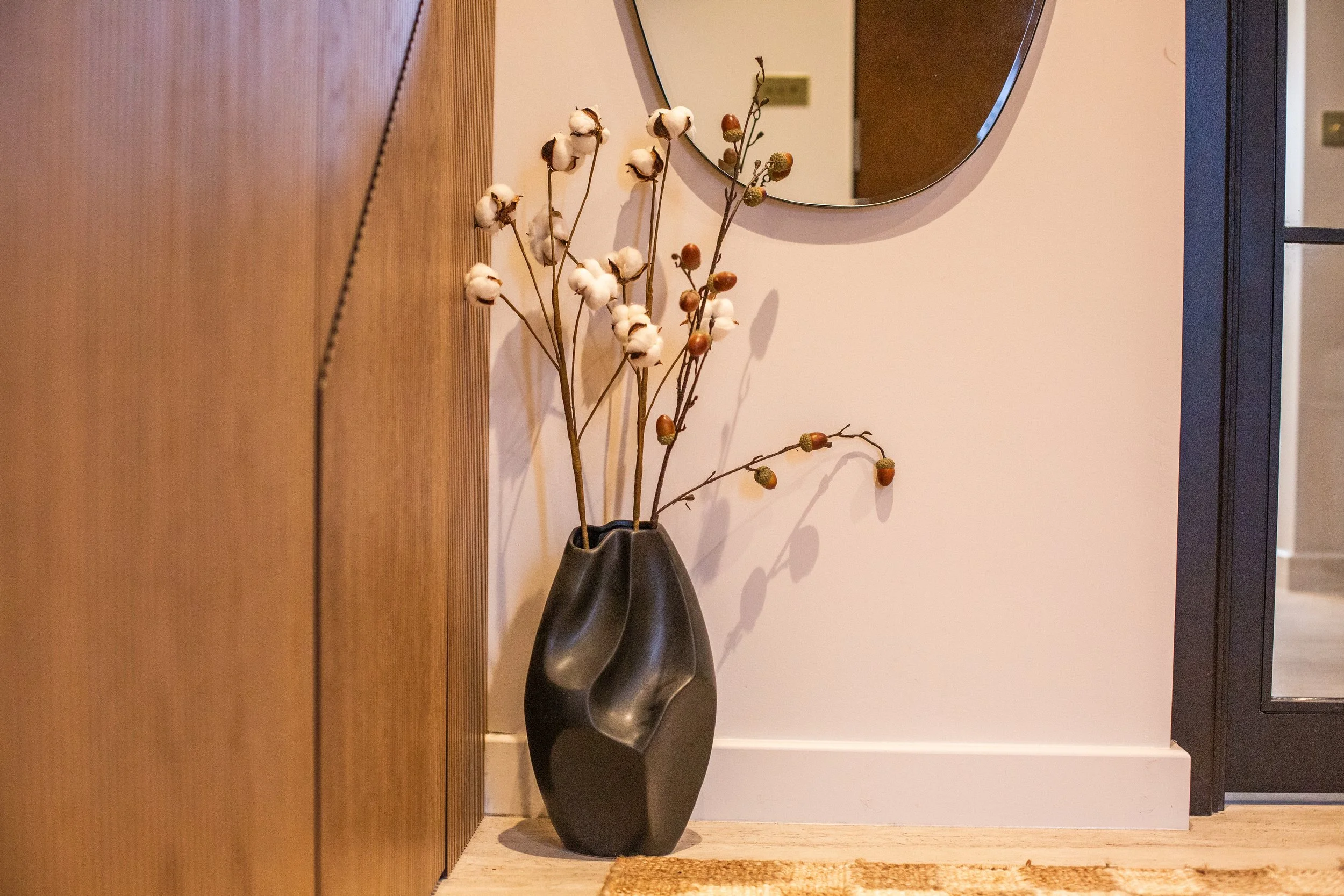 Hidden storage under the stairs with a sculptural black vase, cotton branches and a minimalist mirror, showing how unused space can become functional in modern Cambridge homes.