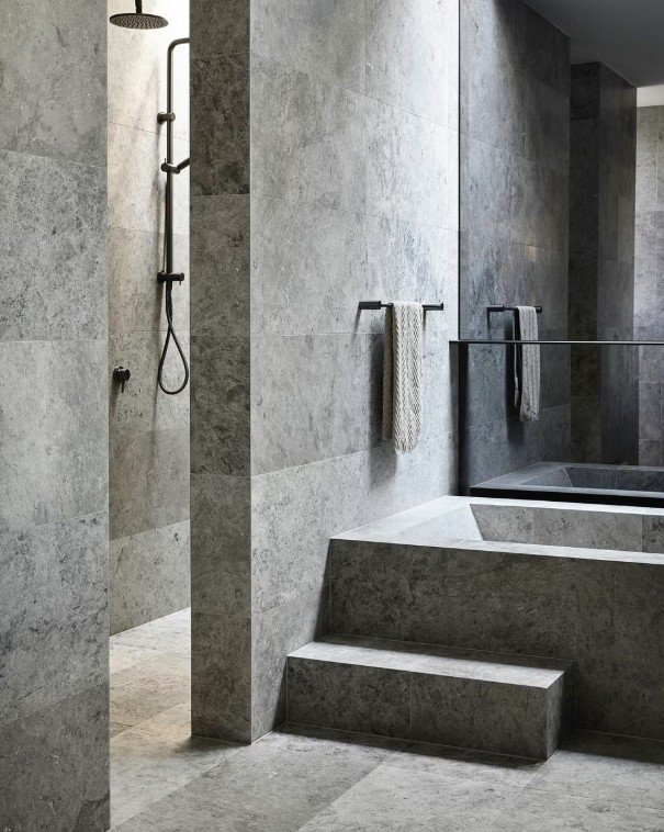 Brutalist bathroom with large stone tiles, black fixtures, built-in bath, and walk-in shower. Photo by Derek Swalwell.