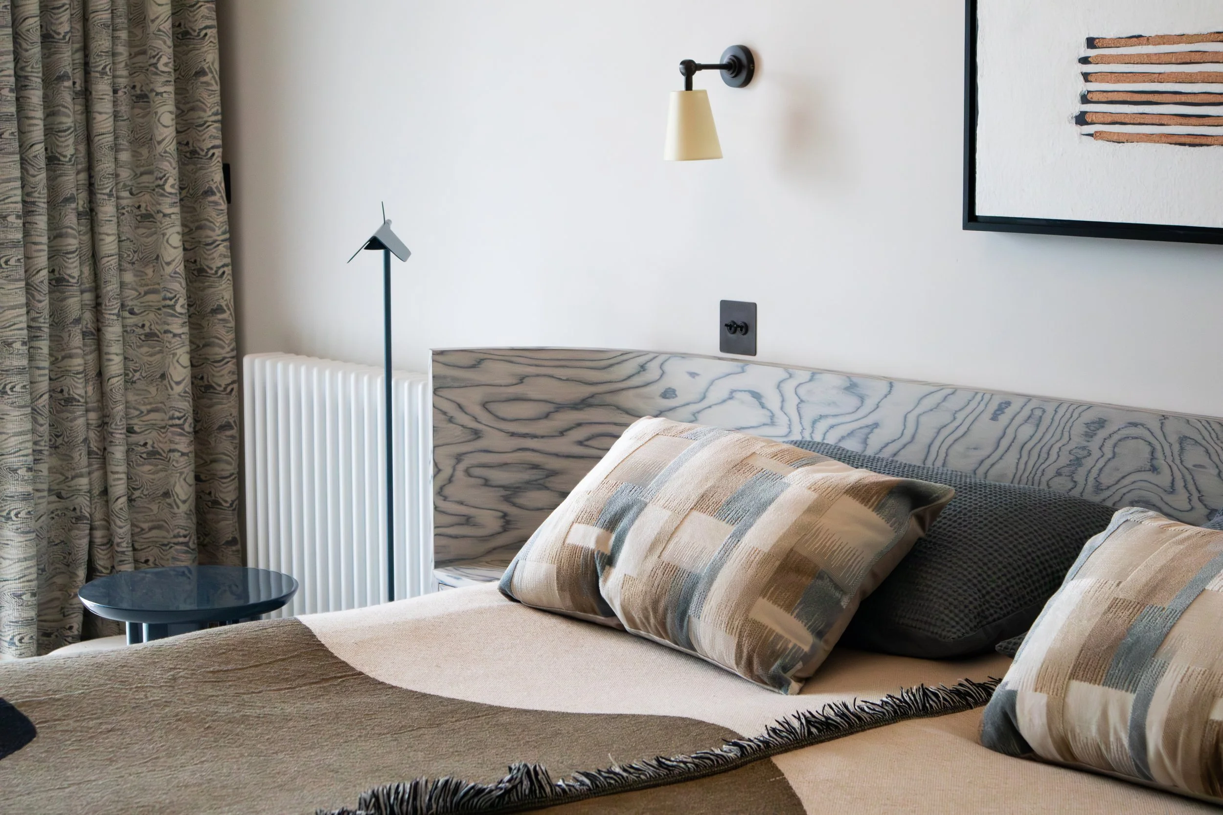 Contemporary bedroom with curved headboard, wood veneer, and layered textiles in a Cambridge home