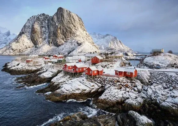 Winter view of Hamnøy fishing village in Norway’s Lofoten Islands, with red rorbu cabins and dramatic mountain backdrop.
