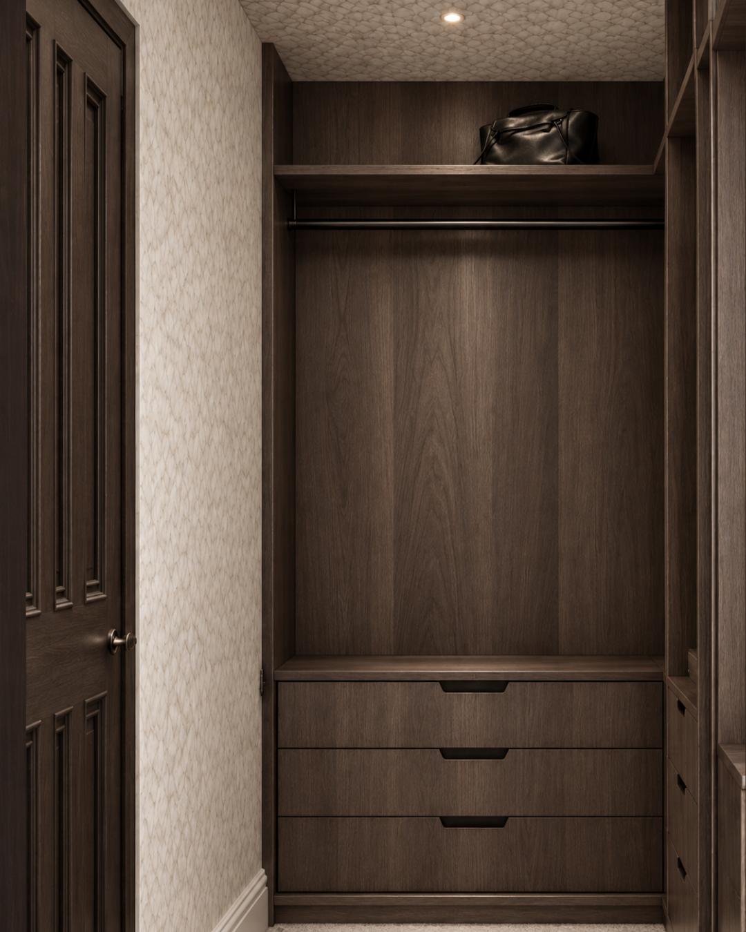 Bespoke dark timber walk-in wardrobe in a Cambridge master bedroom, featuring integrated drawers, open hanging space and warm recessed lighting