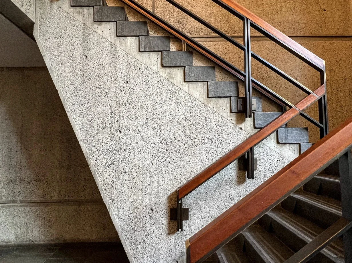 Cantilevered staircase with dark treads and textured concrete wall, inspired by Marcel Breuer’s minimalist architecture.