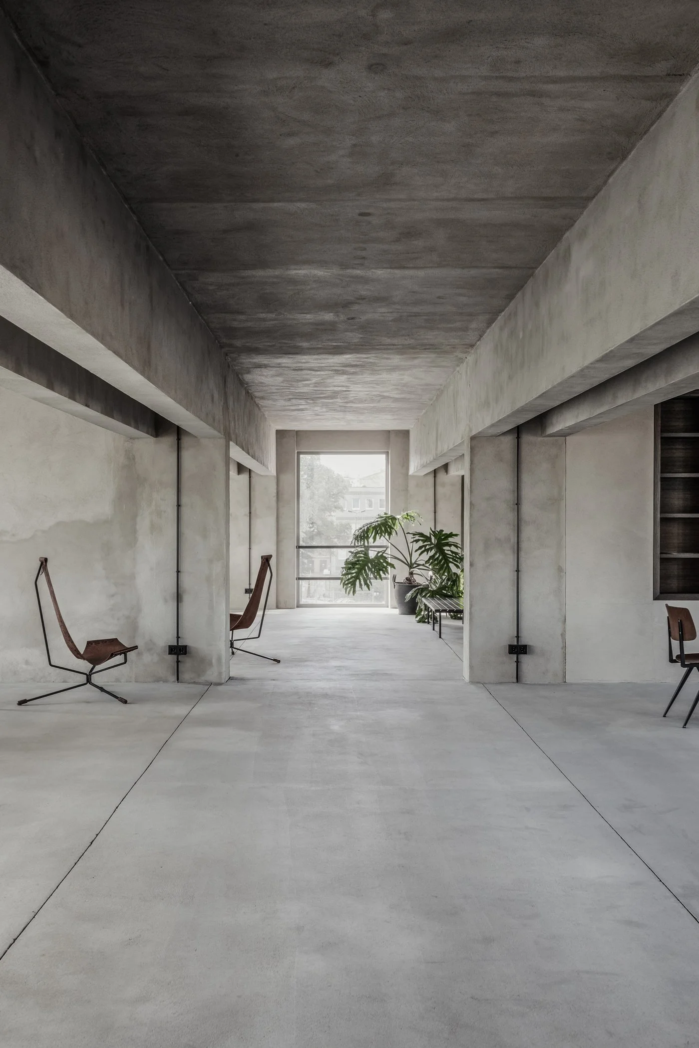 Brutalist interior with exposed concrete walls, leather sling chairs, and potted plant. Photo via Leibal.
