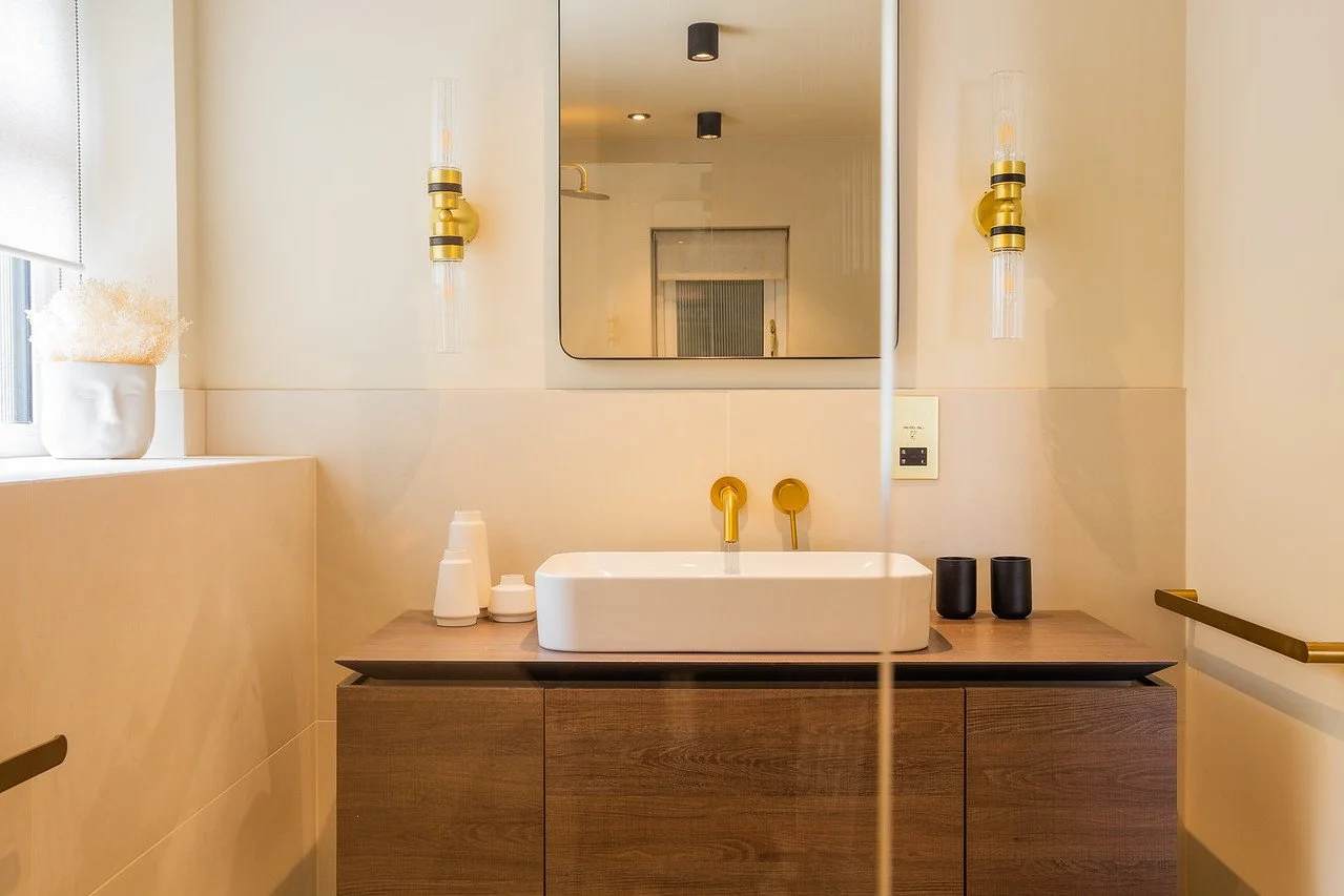 Warm-toned bathroom in Gamlingay featuring a sculptural sink, wall-mounted brass fixtures, and soft lighting.