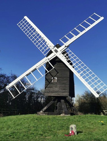 Historic wooden windmill in Great Gransden, Cambridgeshire, with white sails and memorial flowers beneath