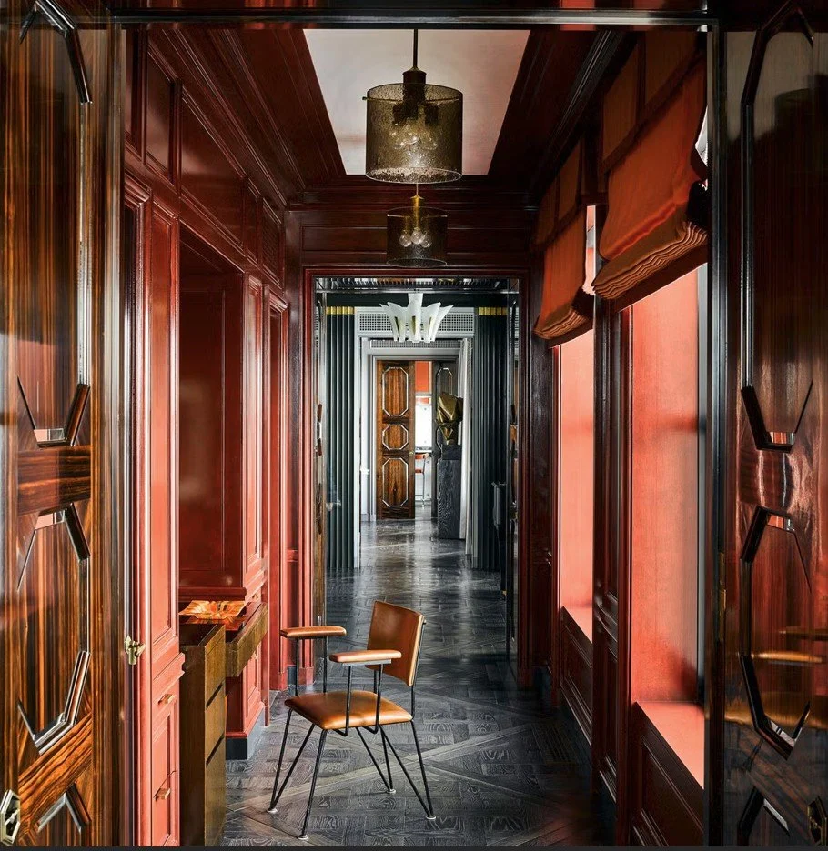 Contemporary Art Deco hallway photographed by Douglas Friedman, featuring glossy red panelled walls, geometric dark‑wood flooring and sculptural modern lighting.