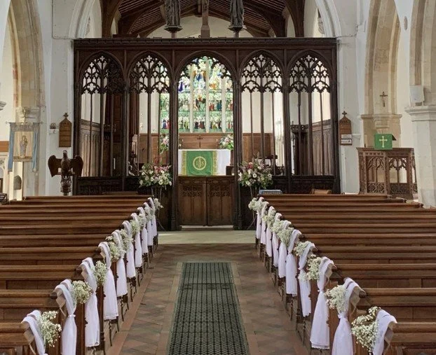 nterior of St Mary the Virgin Church in Gamlingay, Cambridgeshire, with floral pews, Gothic screen, and stained glass.