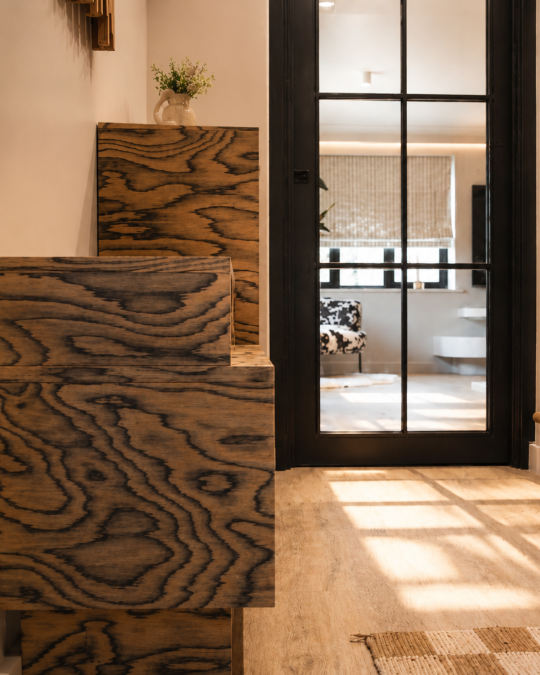 Bespoke hallway joinery designed by Pinterior.space for the Shelford Project, combining distinctive timber grain with integrated storage and a black-framed glazed door connecting the entrance hall to the adjoining living space.