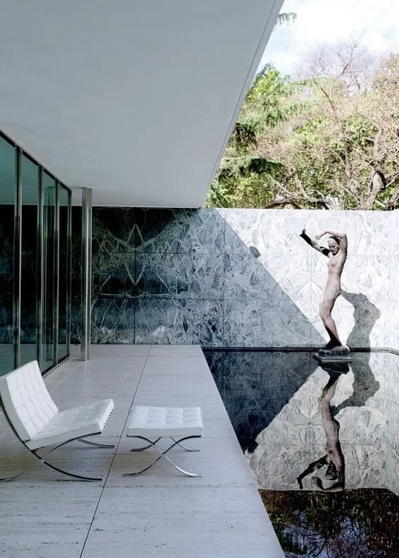 Modernist chair and ottoman beside reflective pool and sculpture in Barcelona Pavilion-inspired architectural setting