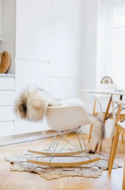 Eames-style rocking chair with fur throw in Nordic kitchen with light wood furniture and floral ru