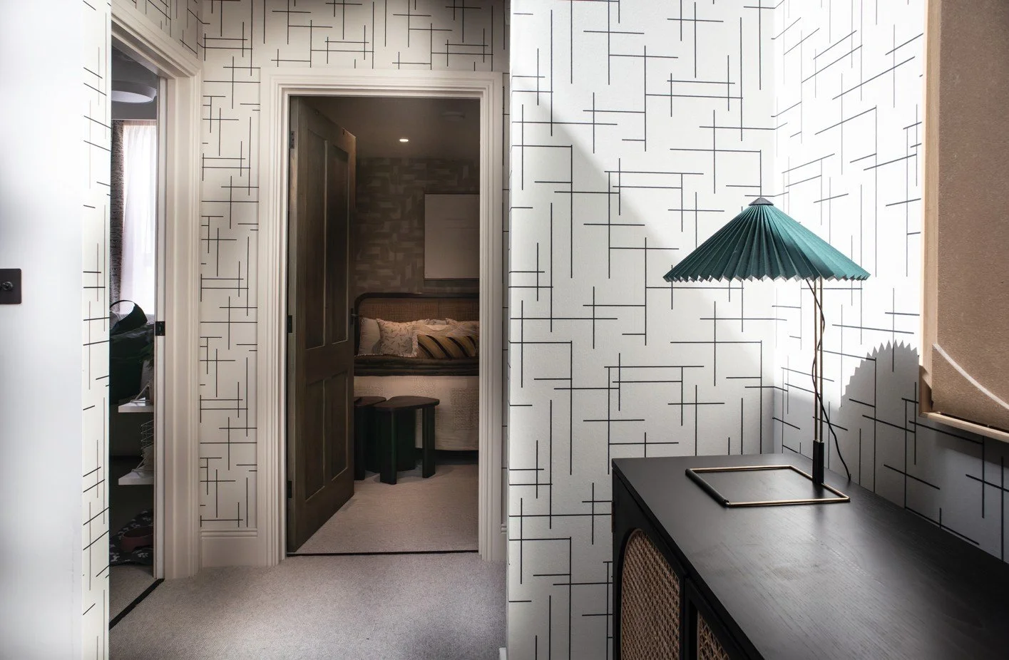 Hallway with geometric wallpaper and pleated lamp leading to guest bedroom in Cambridge Water Lane project