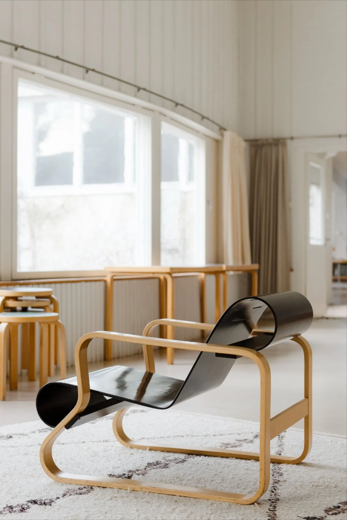Alvar Aalto-inspired lounge chair with curved black seat and light wood frame in Scandinavian interior