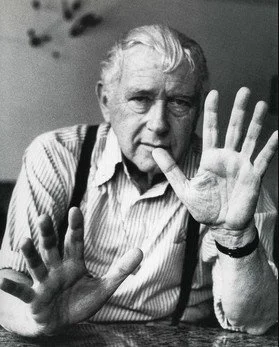 Black-and-white portrait of Marcel Breuer with raised hands, striped shirt and suspenders, seated and expressive.