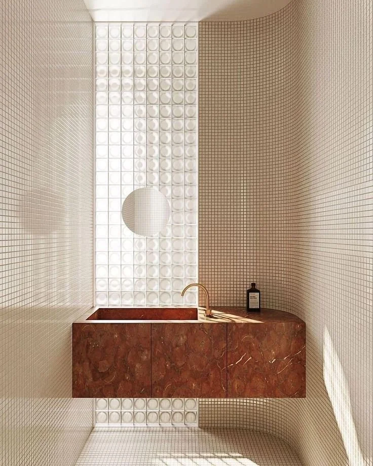 Contemporary London bathroom with light‑reflective glass blocks, small‑format tiling and a brown marble vanity with a modern gold tap.