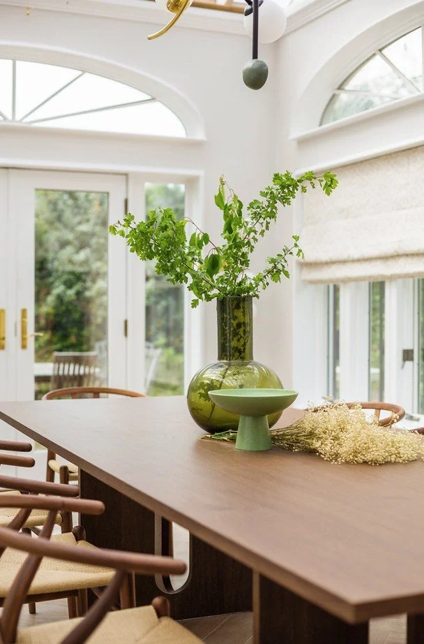 Bright dining room with sculptural lighting, natural wood table, and soft greenery — showing how light shapes atmosphere in Cambridgeshire and London homes.