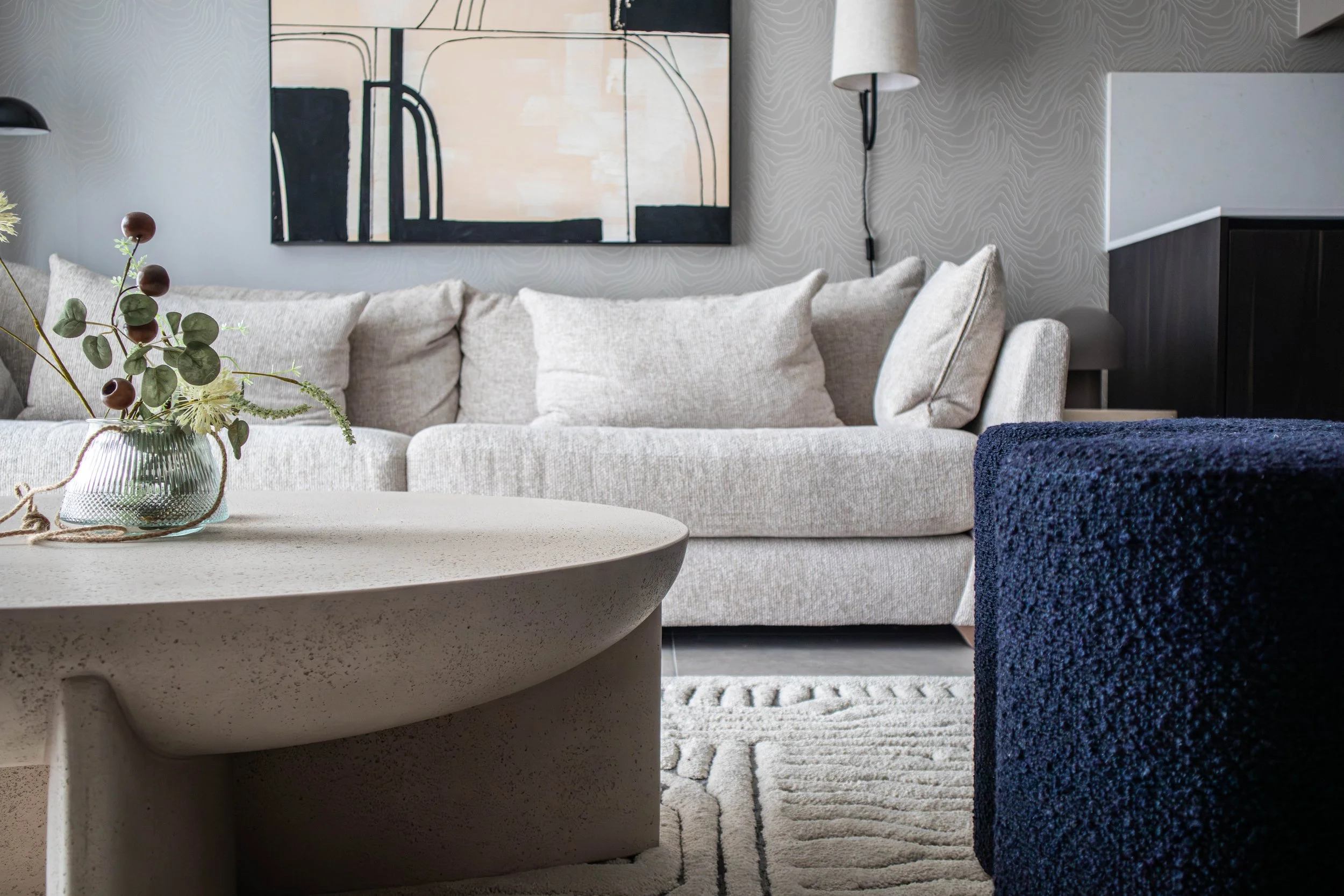 Seating area in the Water Lane living space, featuring a Ferm Living wall light, a textured round coffee table from West Elm, and soft neutral upholstery set against the patterned wallpaper
