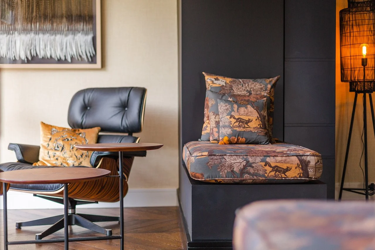 Modern lounge with leather chair, scenic bench cushions, herringbone floor, and abstract artwor