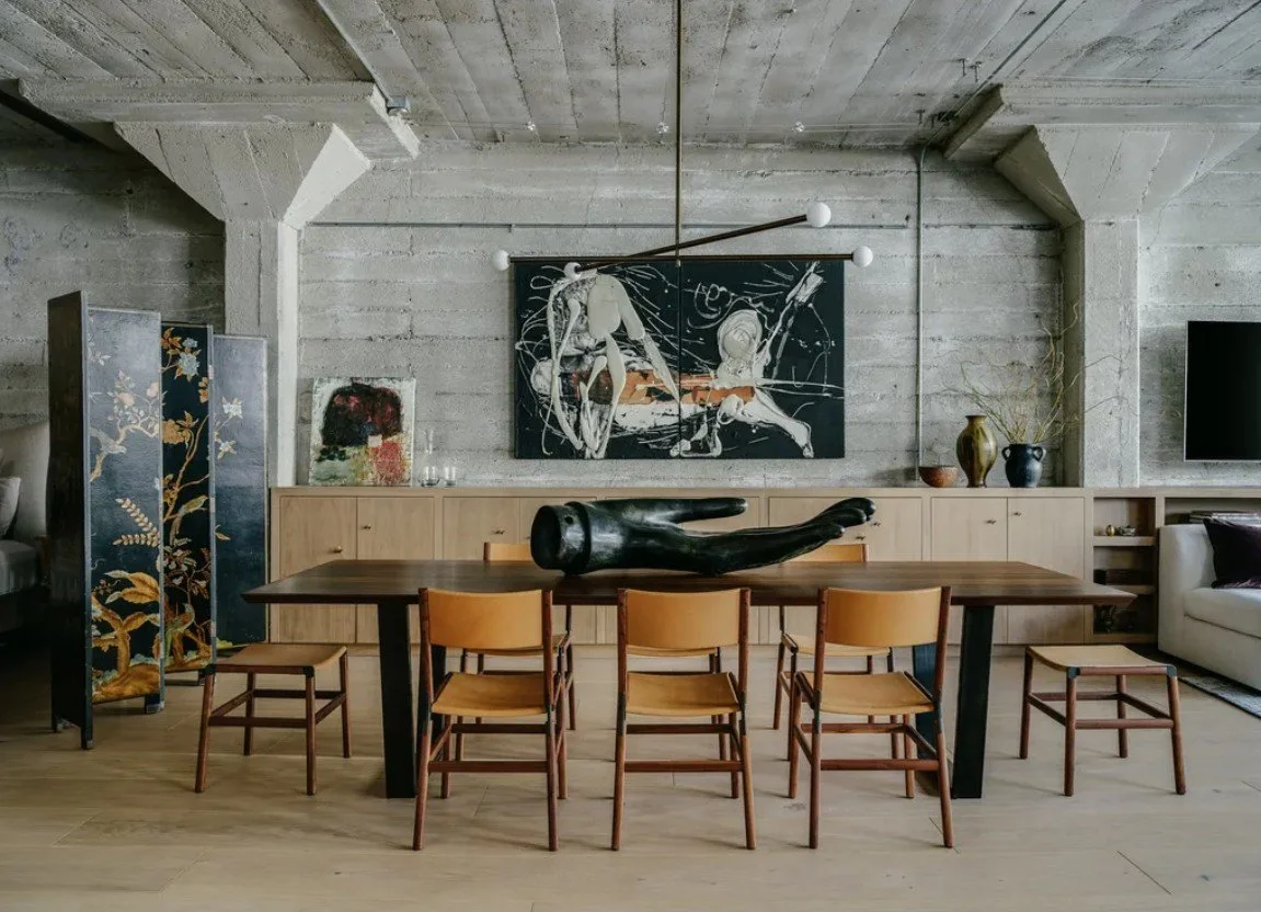 Concrete dining room with timber table, tan leather chairs, abstract sculpture, and eclectic Brutalist decor. Design by Lane McNab Interiors. Photo by Christopher Stark