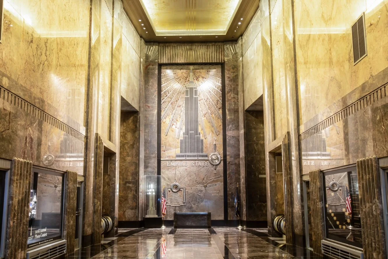 Art Deco lobby of the Empire State Building with a stylised metal mural, geometric stone walls and radiating decorative lines