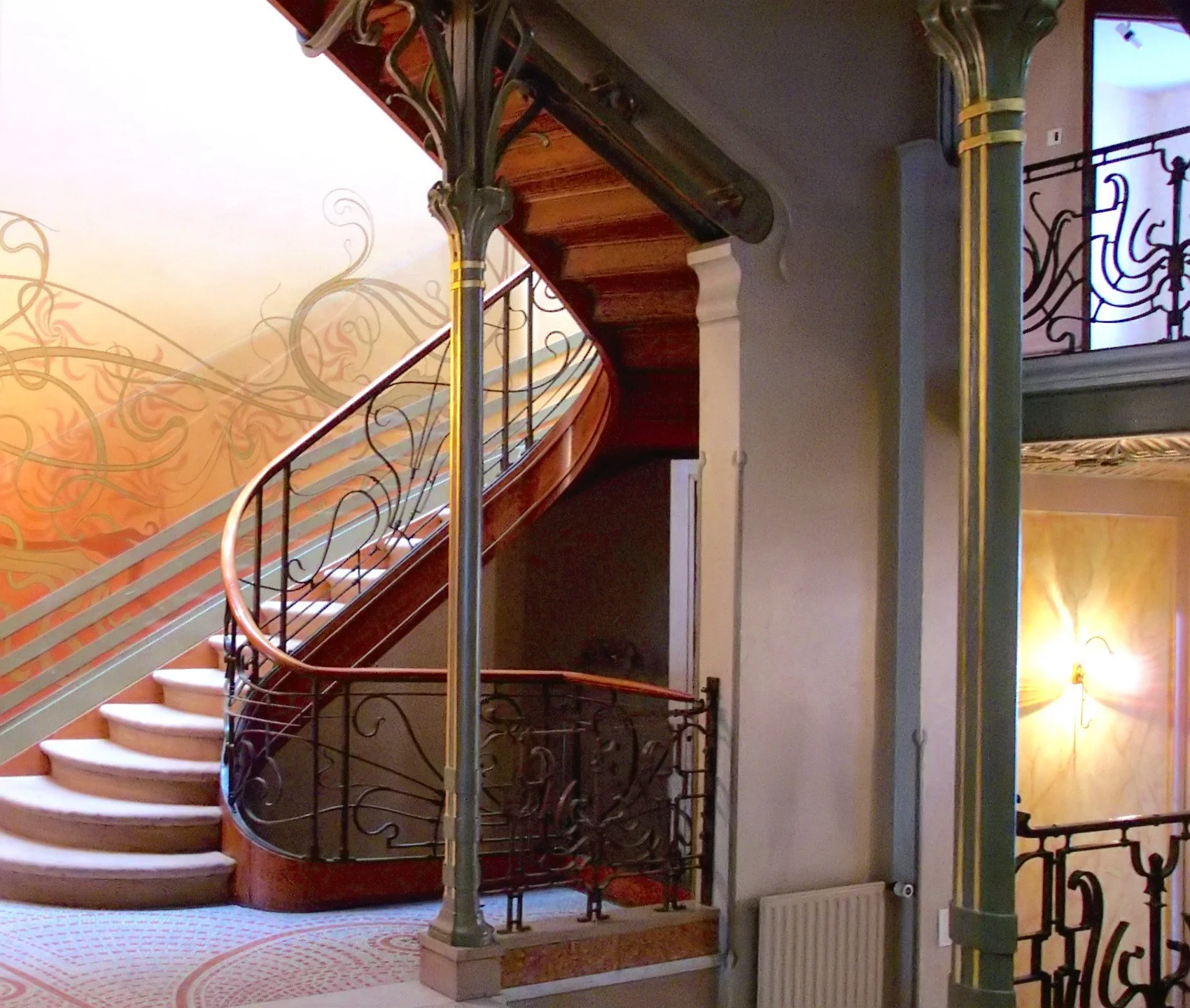 Art Nouveau staircase at Victor Horta’s Hôtel Tassel with flowing wrought‑iron railings, curved wooden steps and organic wall motifs.