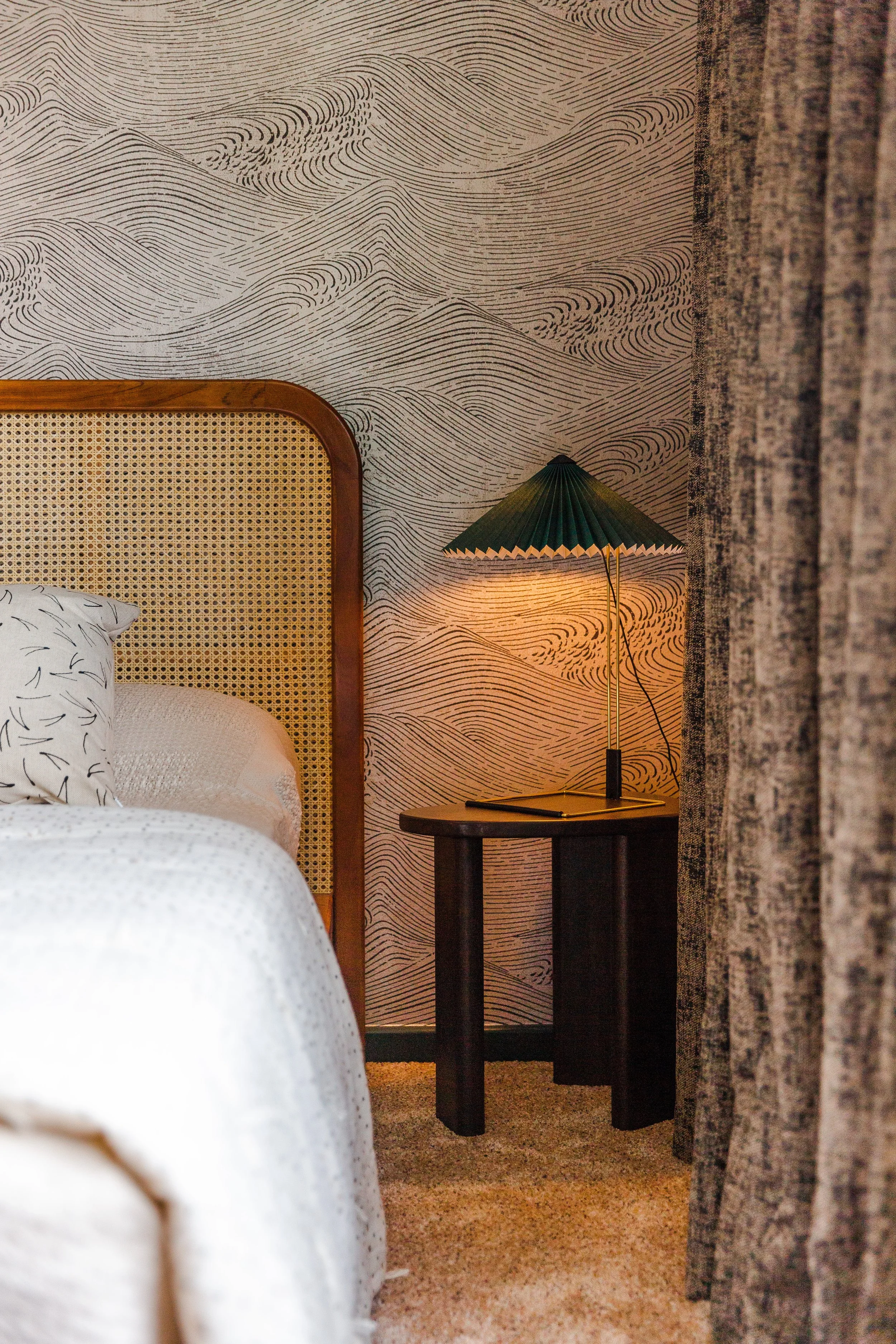Japandi guest bedroom detail from the Gamlingay renovation, showing rattan headboard, sculptural side table, and pleated green lamp.